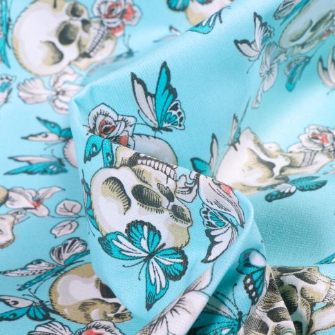 Tissu Coton enduit Têtes de mort et papillons sur fond Bleu turquoise